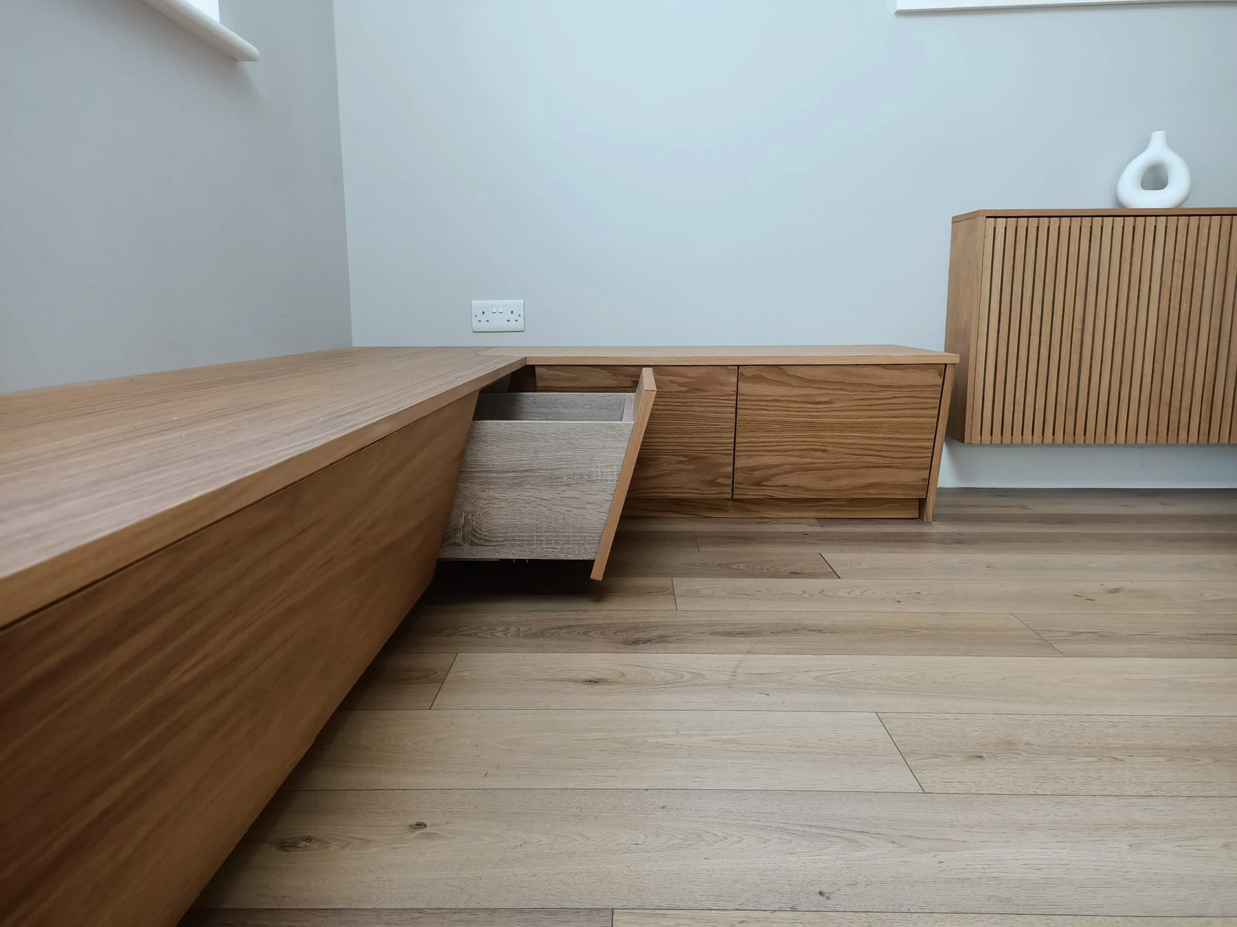 An open drawer beneath the bench seat, beside the matching radiator cover