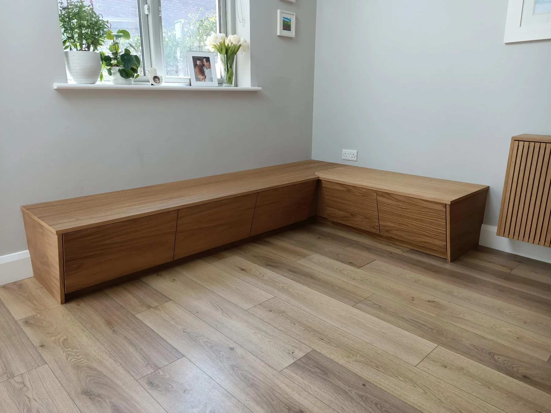 Timber bench seating fitted around a corner, with storage below and a slatted radiator cover alongside