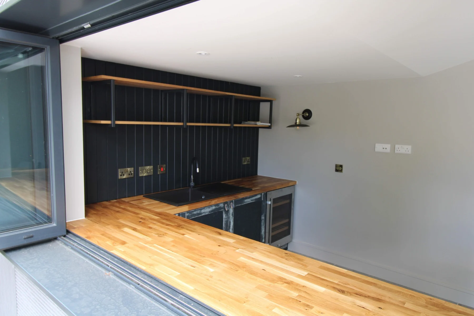 Oak butcher-block worktop meeting the window opening, with the panelled backing and shelving beyond