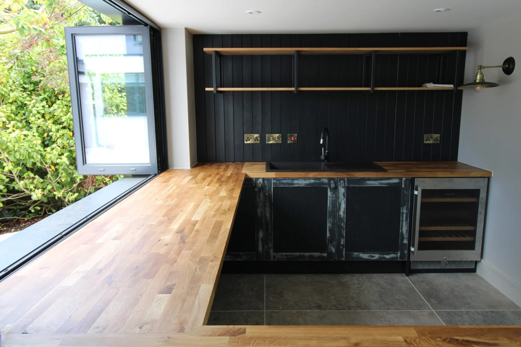 Oak butcher-block worktop running beneath the open windows towards the sink and painted cupboards