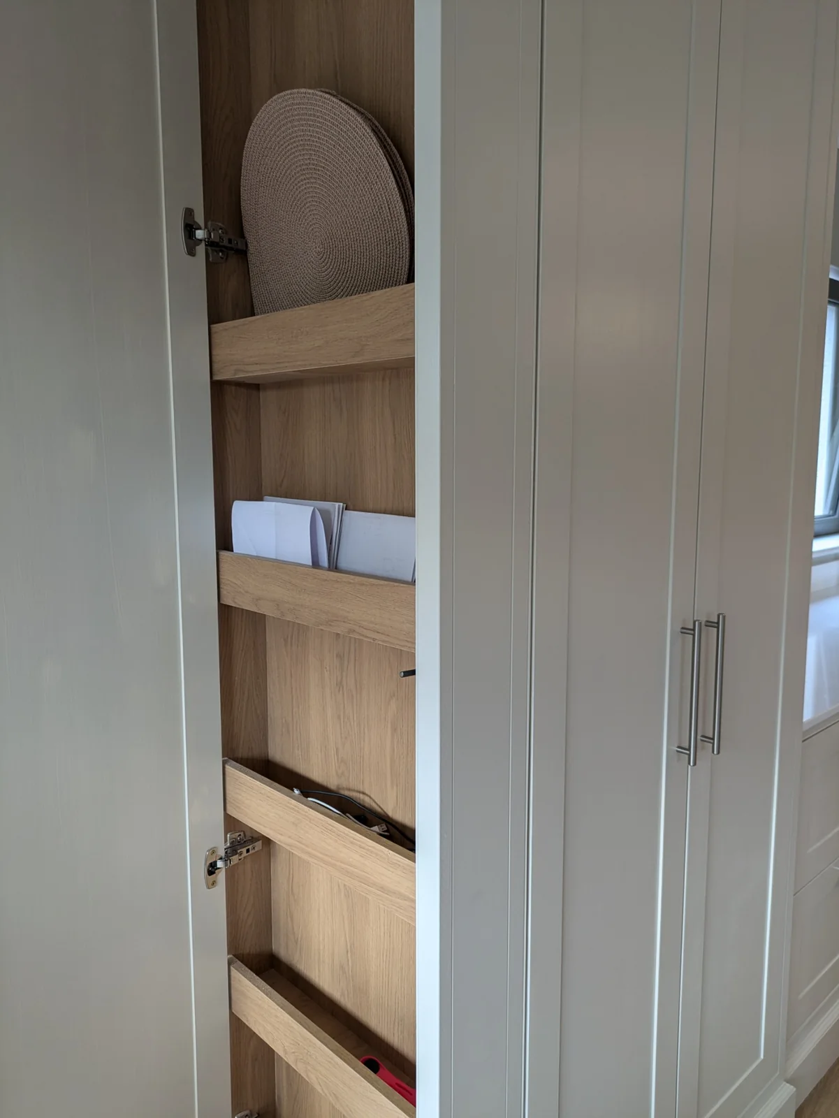 Shallow oak storage racks on the inside of a tall cupboard door