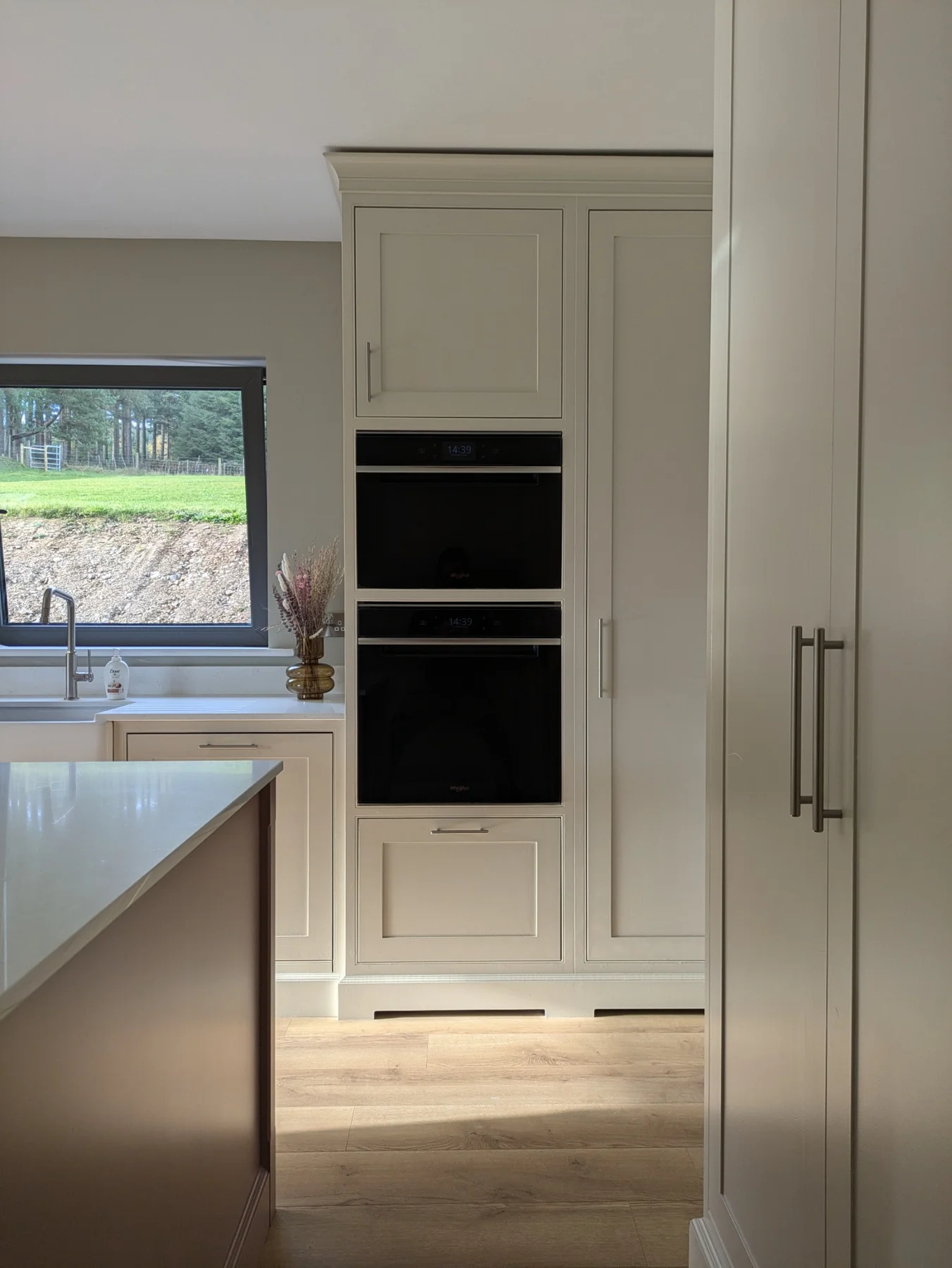 Painted kitchen cabinetry around the window and tall oven cupboard