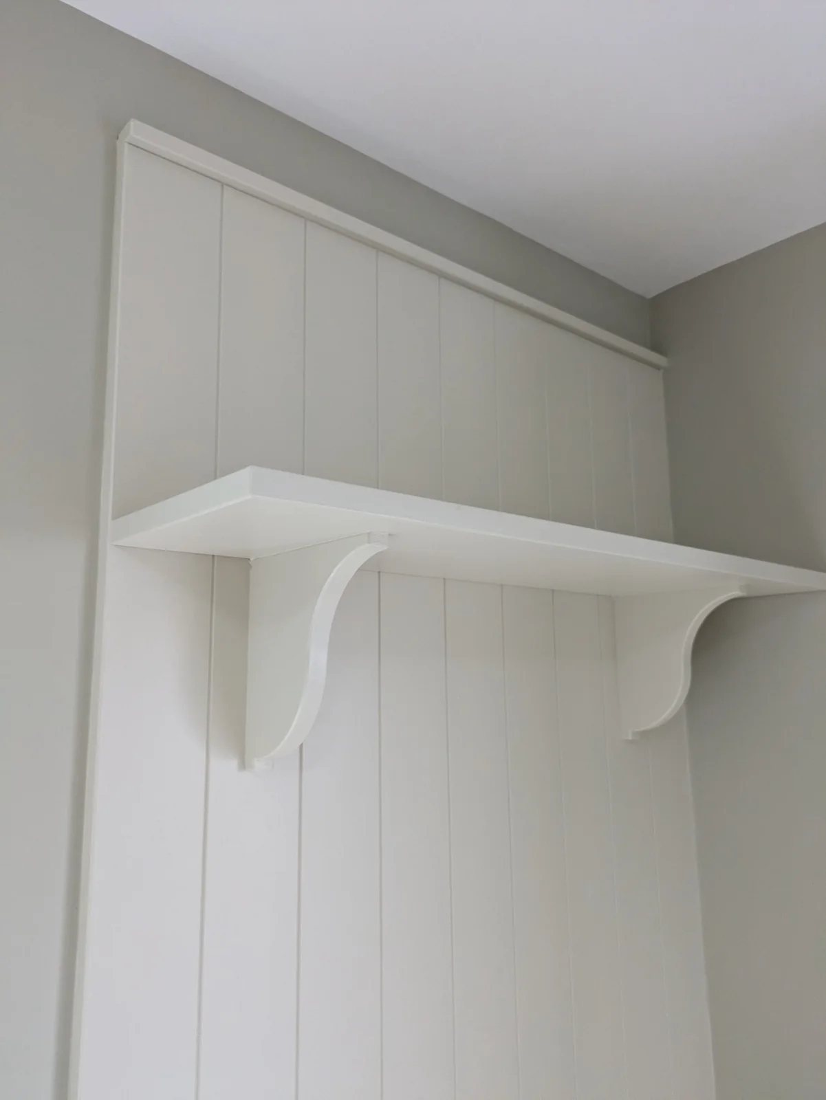 A painted shelf with shaped brackets against panelled backing