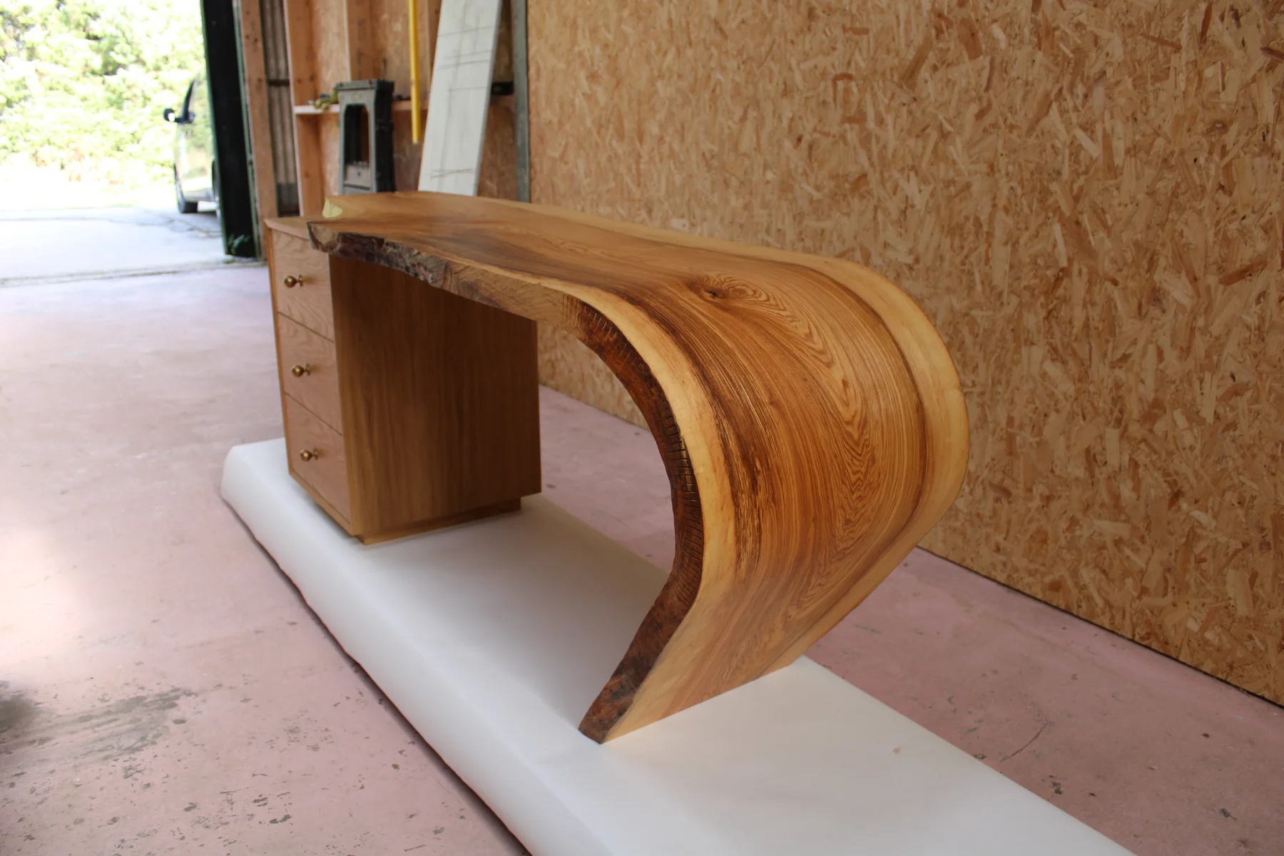 The oak desk viewed from the curved end, showing the solid slab and kerf cuts