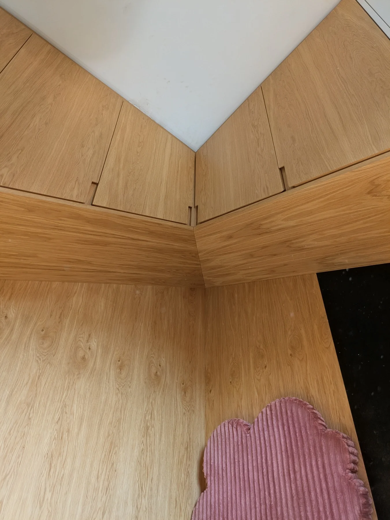 Oak veneer overhead cabinets meeting at the corner above the bed