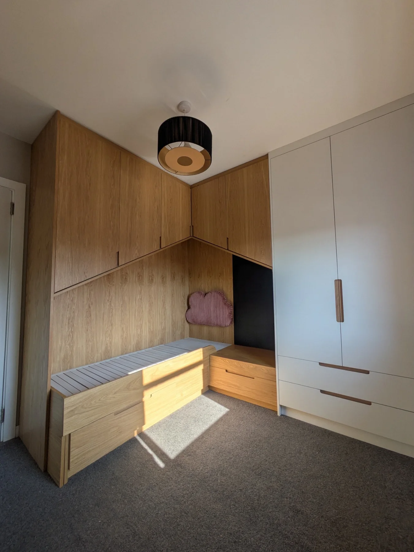 A fitted oak bed and wardrobe with painted doors and angled overhead cupboards