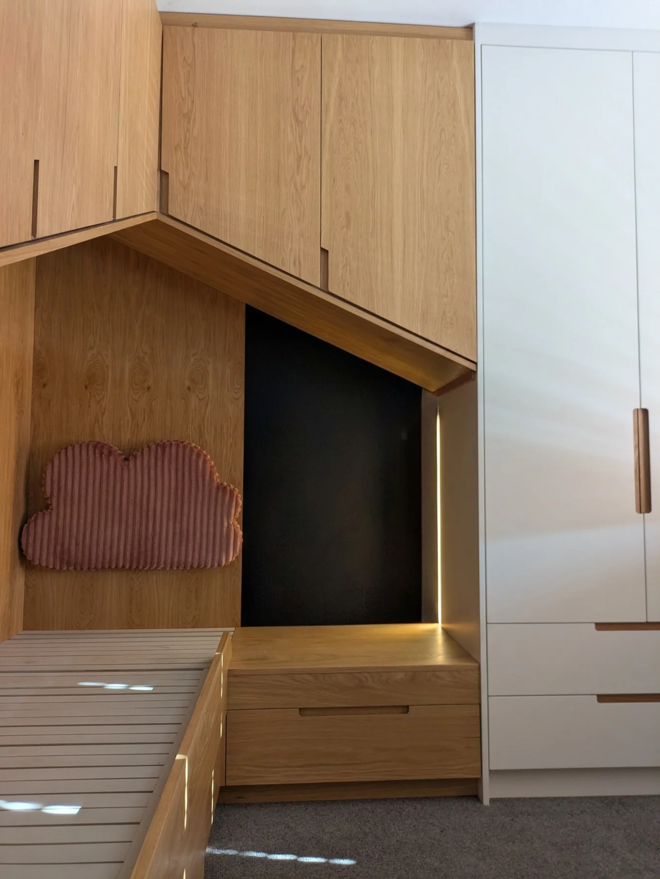 The oak bed frame and bedside drawers beneath angled overhead cabinets