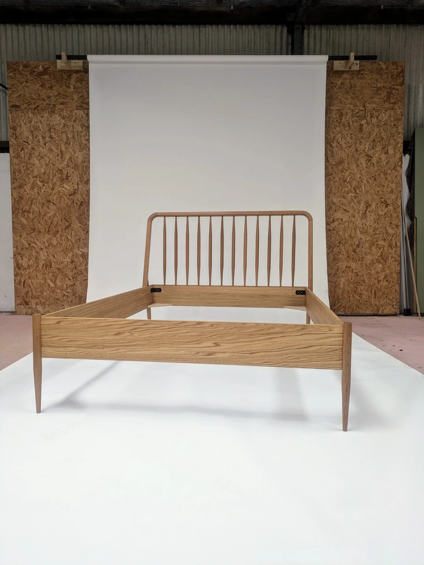 A complete oak bed frame with a spindle headboard and slender legs