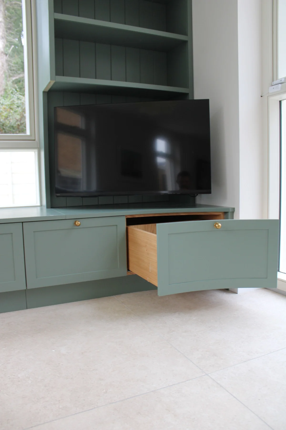 An open drawer beneath the TV in the painted fitted unit