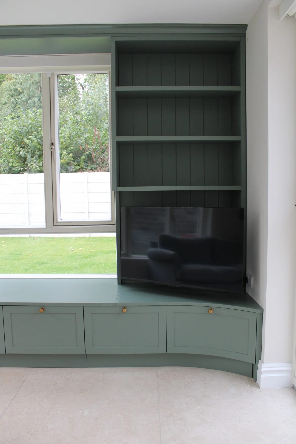 The TV and shelves above curved painted storage cupboards