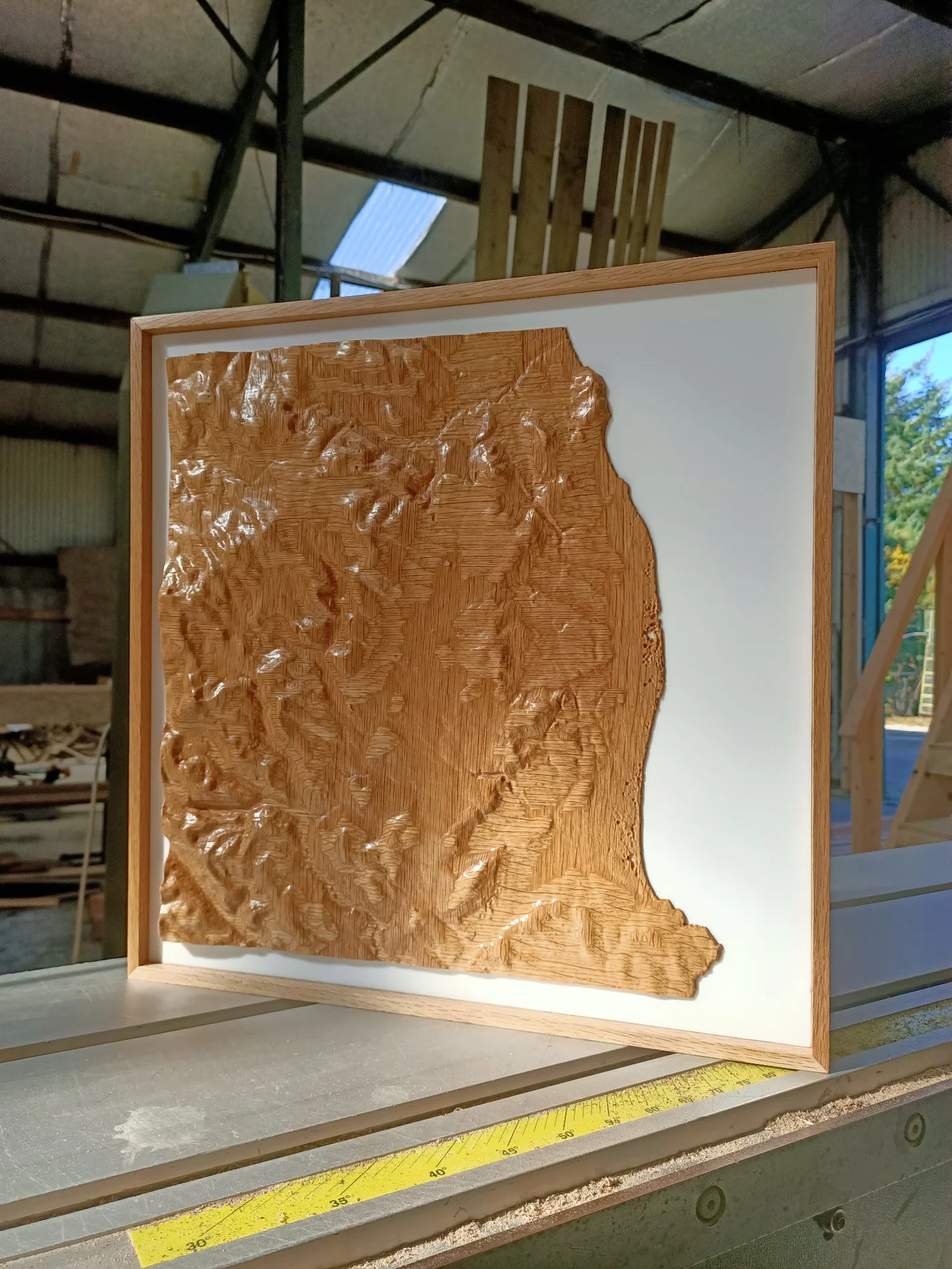 A framed wooden landscape relief with a white backing, viewed at an angle