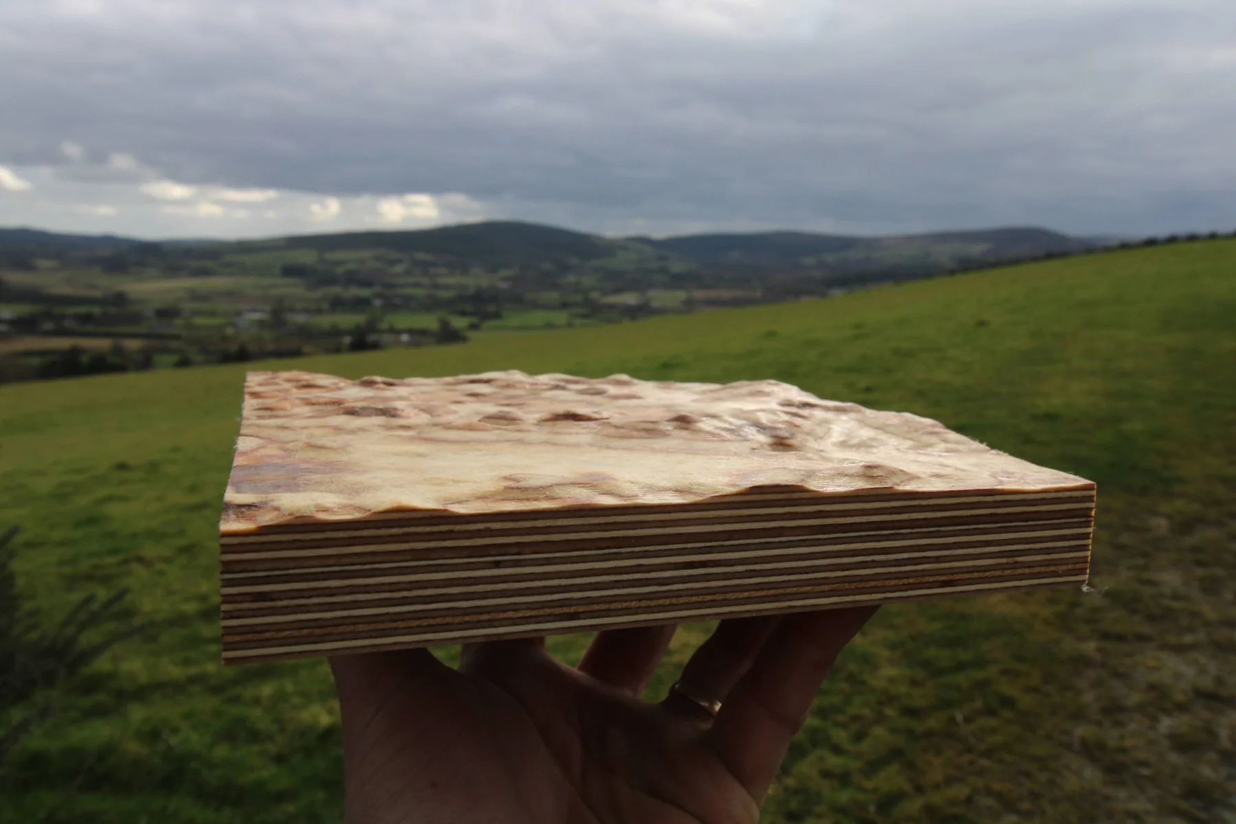 A small wooden terrain model held in front of the surrounding hills and valley