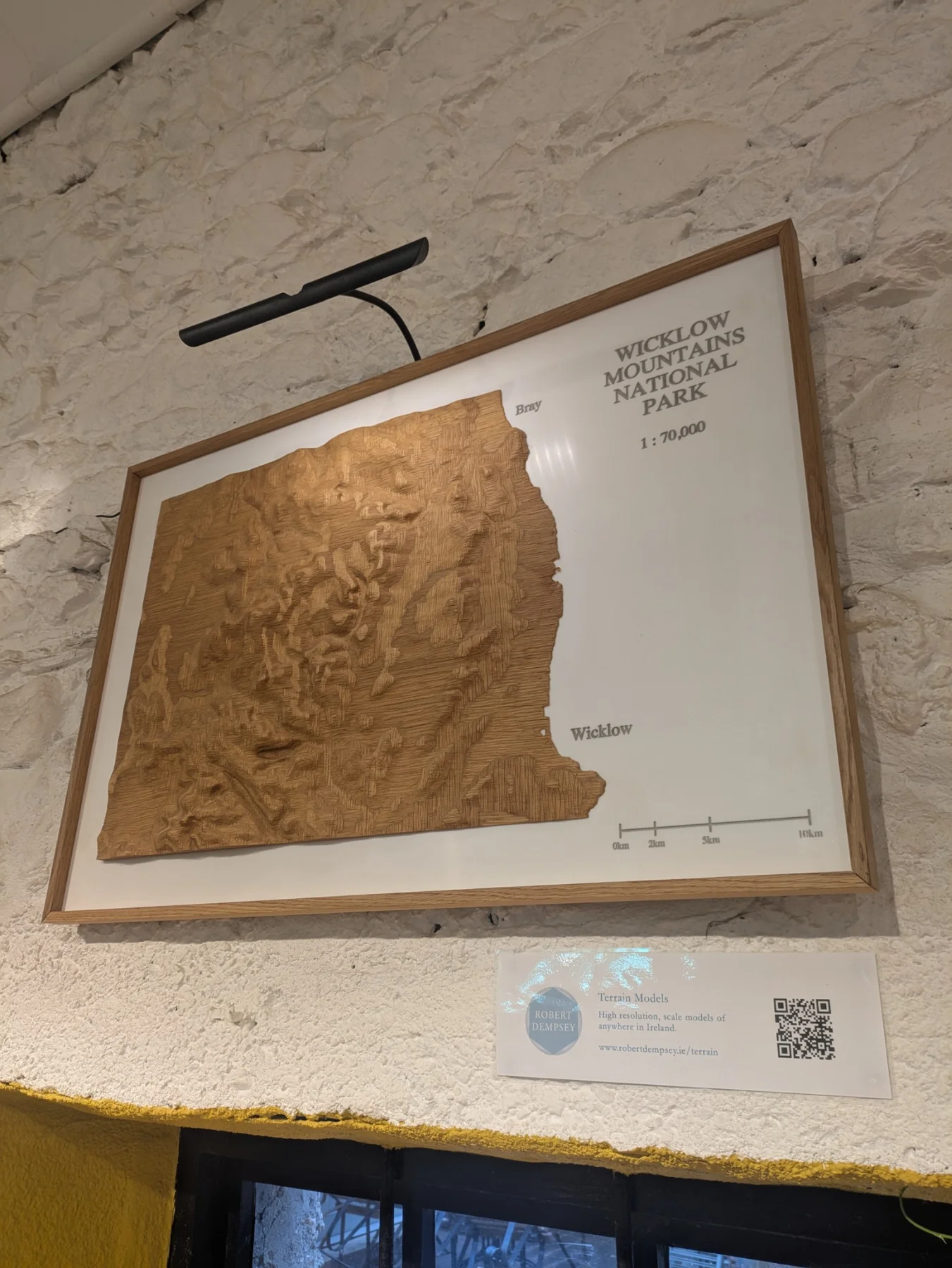 A framed wooden terrain model displayed on a stone wall