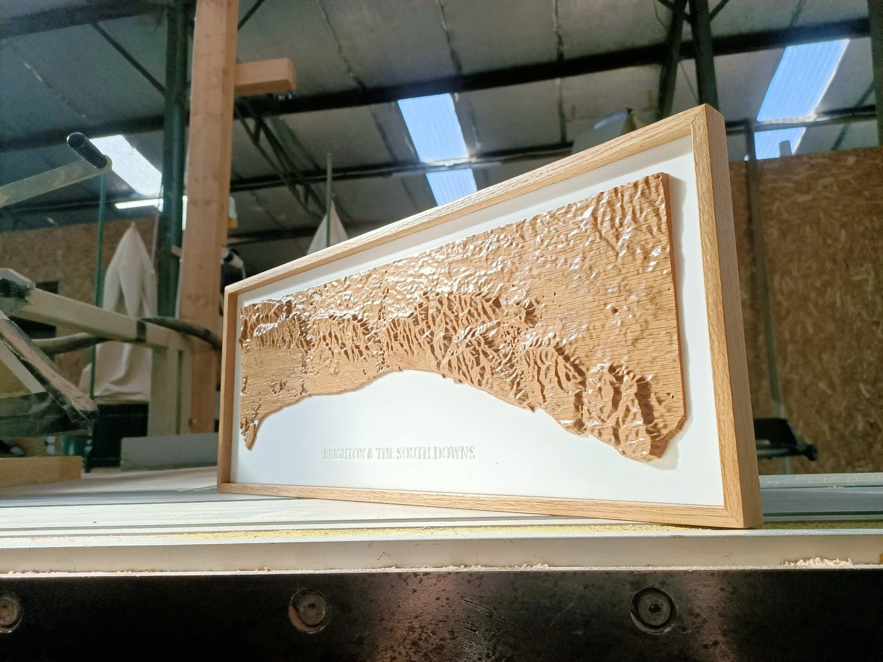 A wide wooden landscape relief on a white backing in a timber frame