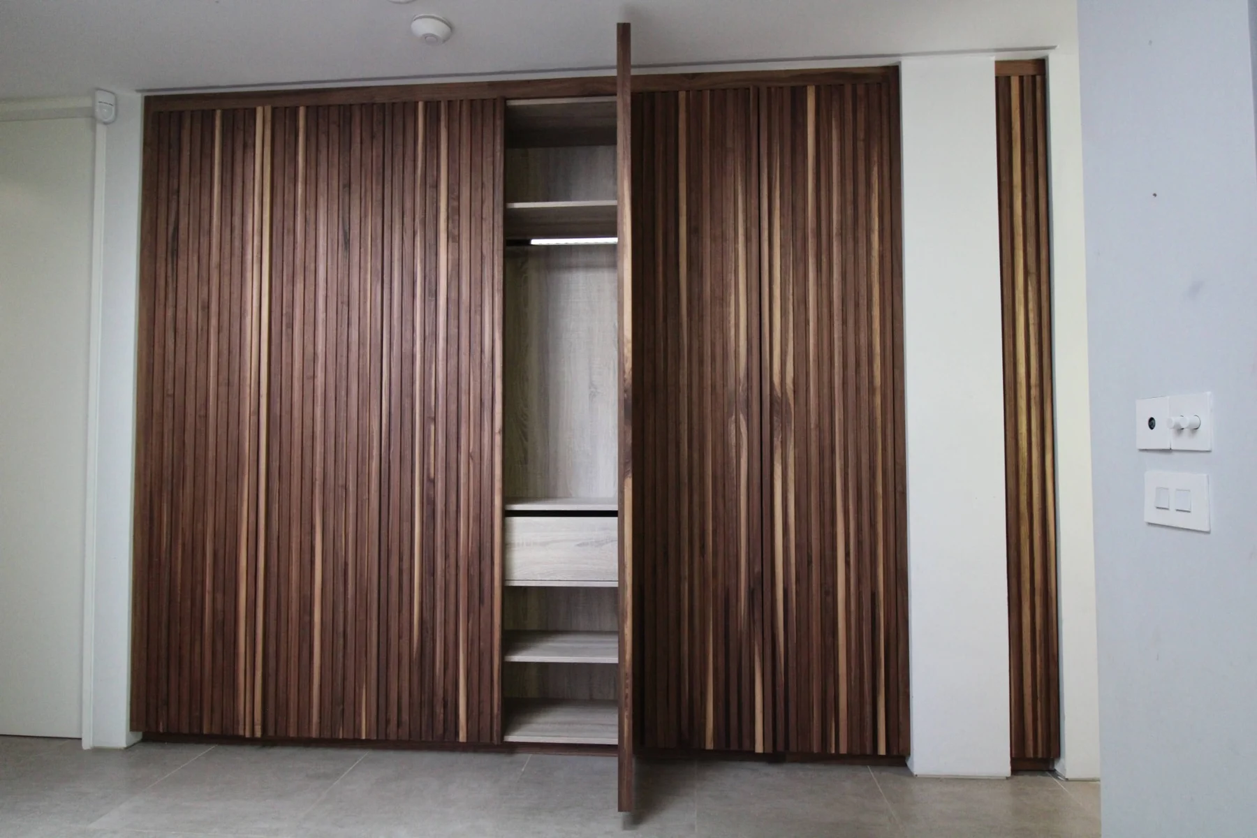 An open walnut slatted door revealing shelves and a hanging rail
